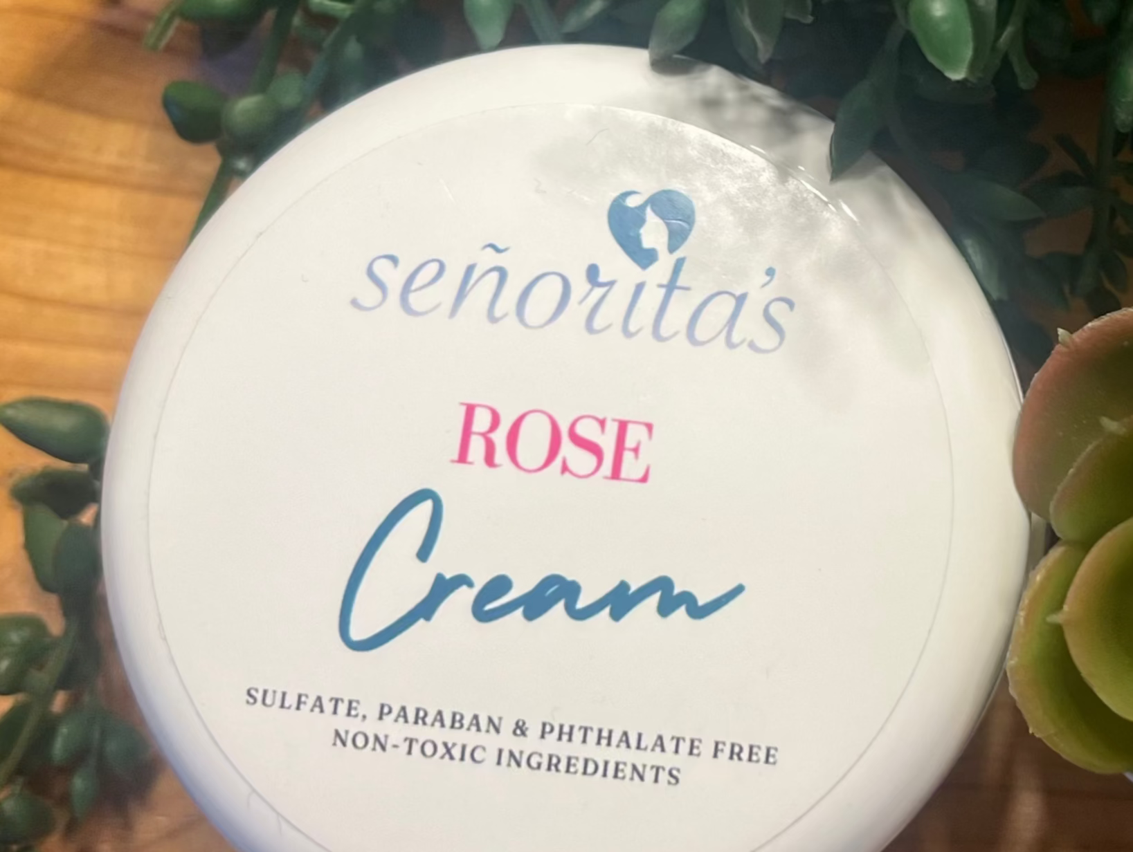 


Container of Senorita's Rose Cream on a wooden surface with greenery and a towel.